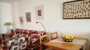 Een woonkamer met een gestreept sofa, een houten eettafel met een mand vol citroenen, en ingelijste foto's aan de muur.