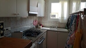 Een keuken met een gasfornuis, oven en spoelbak. Er is een raam met gordijnen en uitzicht op de omgeving.