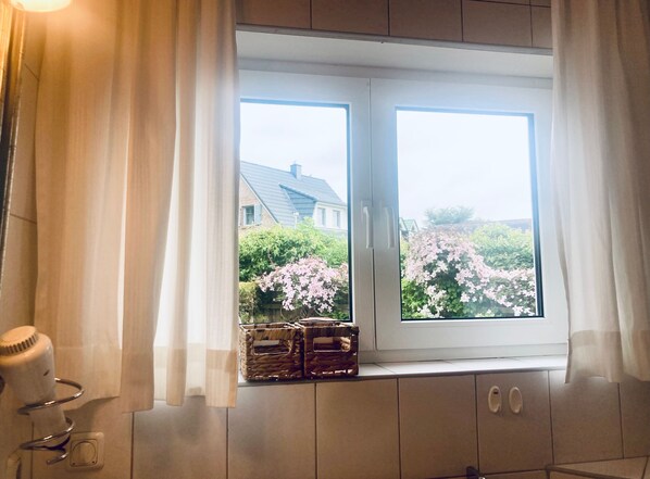 Une salle de bain avec une fenêtre, un sèche-cheveux et un panier posé sur le rebord de la fenêtre.