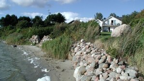 Una propiedad costera con un muro de piedra, una casa junto a una roca grande, y un cielo despejado.