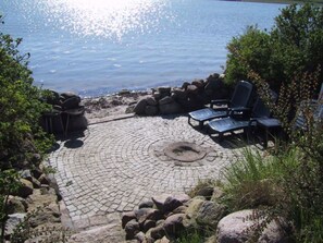 Une terrasse circulaire en pierre, dotée de chaises longues et d’un foyer, qui offre une vue sur une étendue d’eau.