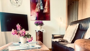 Una sala de estar con una mesa de centro de madera, un sofá de cuero negro, un reloj en la pared y un cuadro.