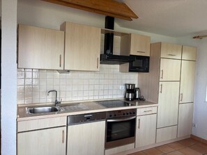 A compact kitchen with light wood cabinets, a stainless steel sink, a microwave, a stove, and a coffee maker.