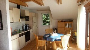 A kitchen with white cabinets, a dining table with chairs, and a window with a view of greenery. - Apartment Amrhein Hinterm Deich OG - Apartments Amrhein Hinterm dike (Kappeln)