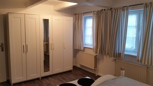 A bedroom with a wardrobe, a window with curtains, a radiator, and a bed. - Apartment Amrhein Hinterm Deich OG - Apartments Amrhein Hinterm dike (Kappeln)