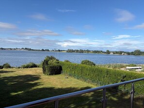 Blick auf einen See mit einer Wiese im Vordergrund und einer fernen Uferlinie mit Gebäuden.