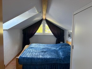 A small bedroom with a sloped ceiling, a single bed, a window with curtains, and a framed picture on the wall.