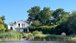 A house by a lake with a balcony, surrounded by trees and vegetation. - Apartment Amrhein Hinterm Deich OG - Apartments Amrhein Hinterm dike (Kappeln)