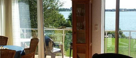 A room with a dining table, chairs, a cabinet, and large sliding glass doors leading to a balcony with a view of a lake.