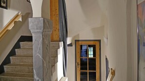 Eine Treppe mit Marmorsäulen, eine Holztür mit Glasfeldern und ein gerahmtes Bild an der Wand.