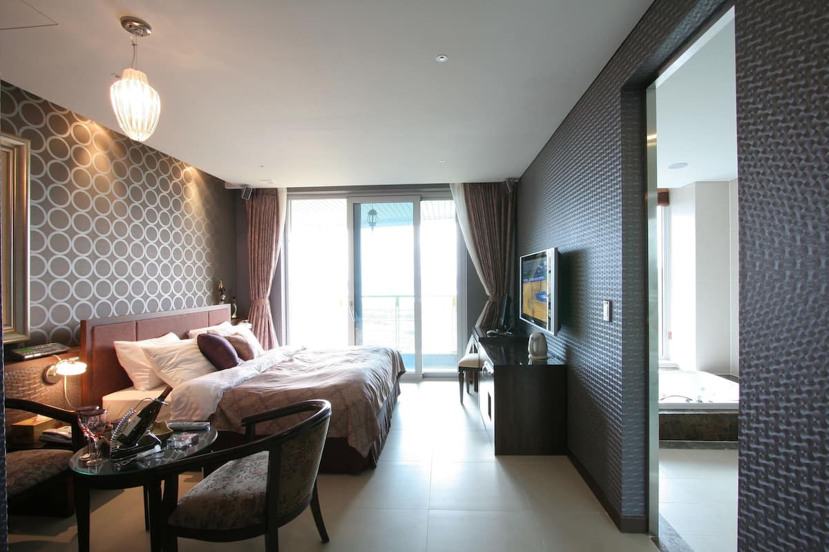 A hotel room with a bed, a desk with a chair, a television, and a large window.