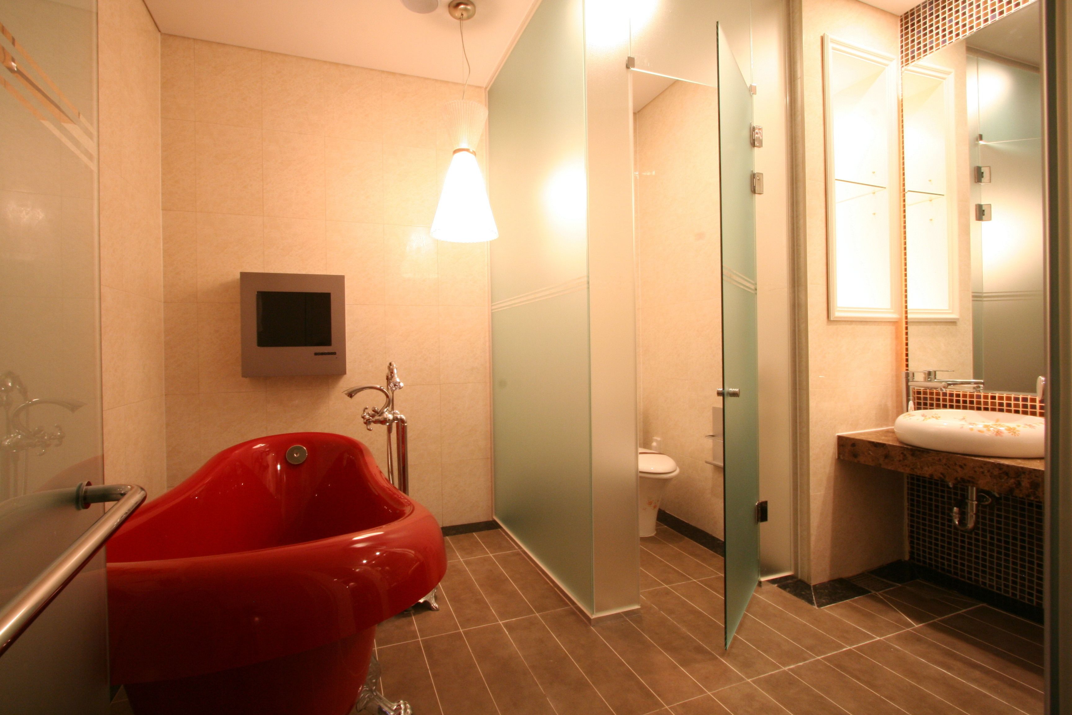 Un baño moderno con una bañera roja, un box de ducha de vidrio, un inodoro y un lavabo con espejo.