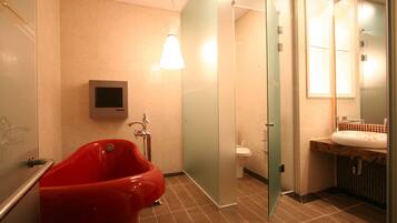 A modern bathroom with a red bathtub, a glass shower enclosure, a toilet, and a sink with a mirror.