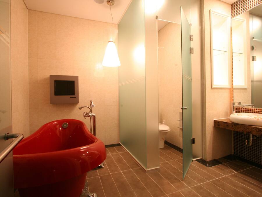 A modern bathroom with a red bathtub, a glass shower enclosure, a toilet, and a sink with a mirror.