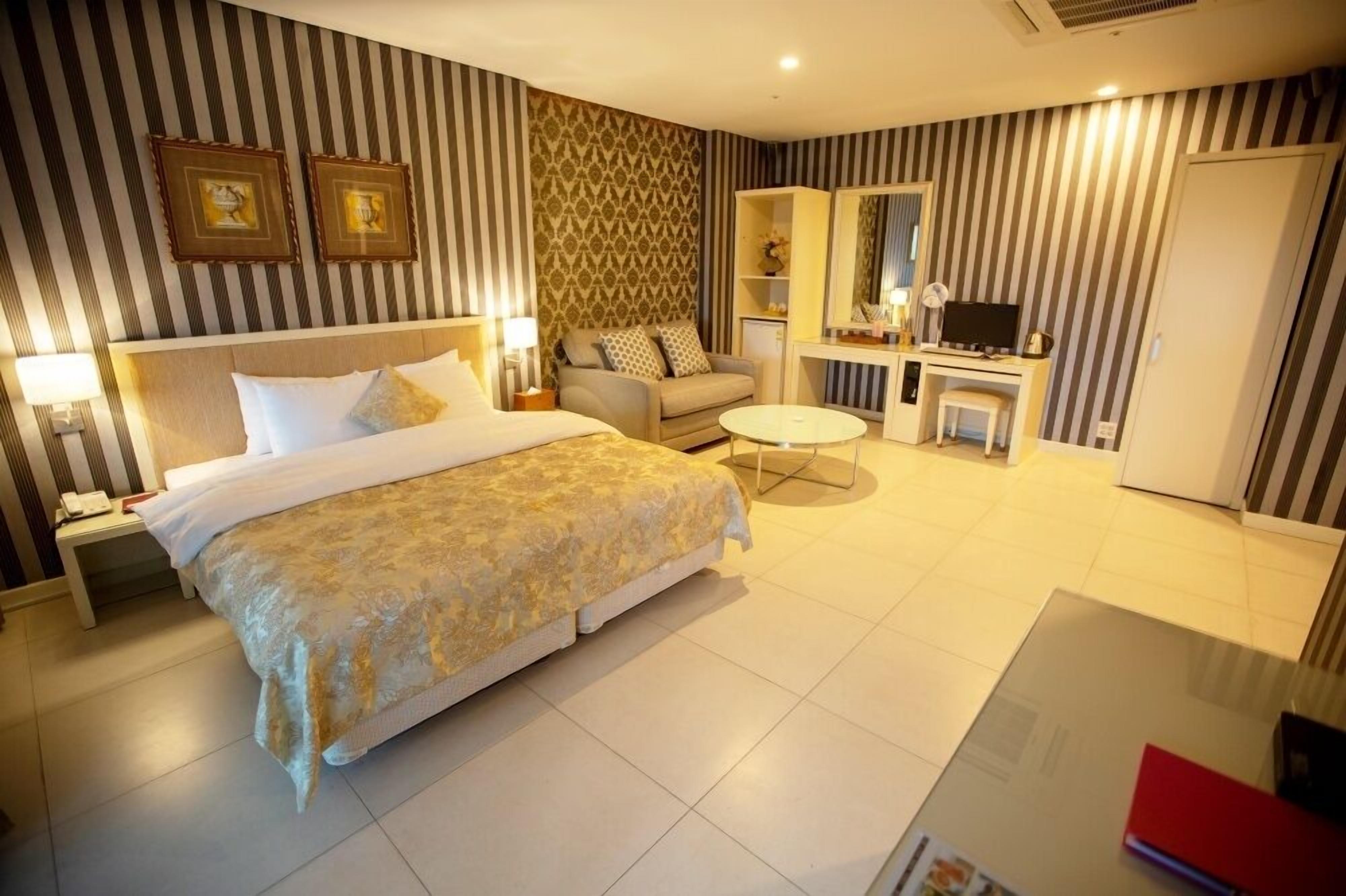 A hotel room with a large bed, a sofa, a small table, a TV, and a desk.