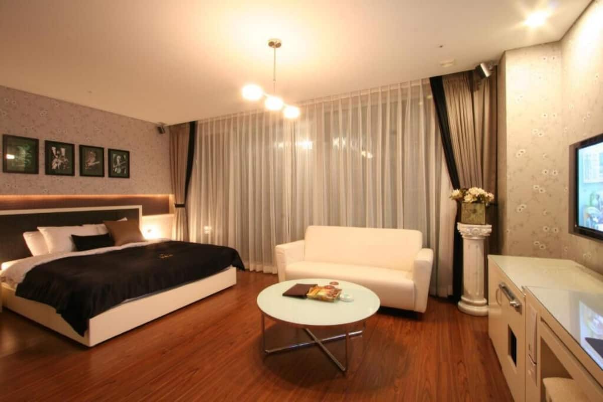 A modern hotel room with a bed, a white sofa, a round coffee table, and a TV.