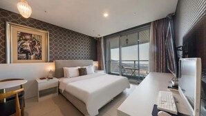 Habitación de hotel con una cama grande, un escritorio con computadora, una mesita pequeña y un cuadro en la pared.