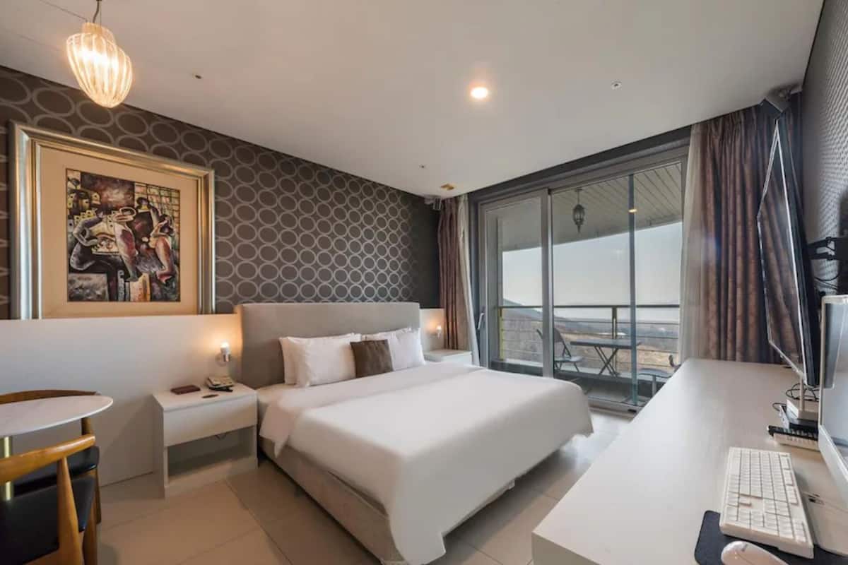A hotel room with a large bed, a desk with a computer, a small table, and a painting on the wall.