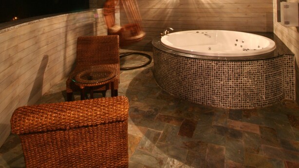 Un cuarto de spa con techo de madera, bañera de hidromasaje, mobiliario de mimbre y una lámpara de pared.