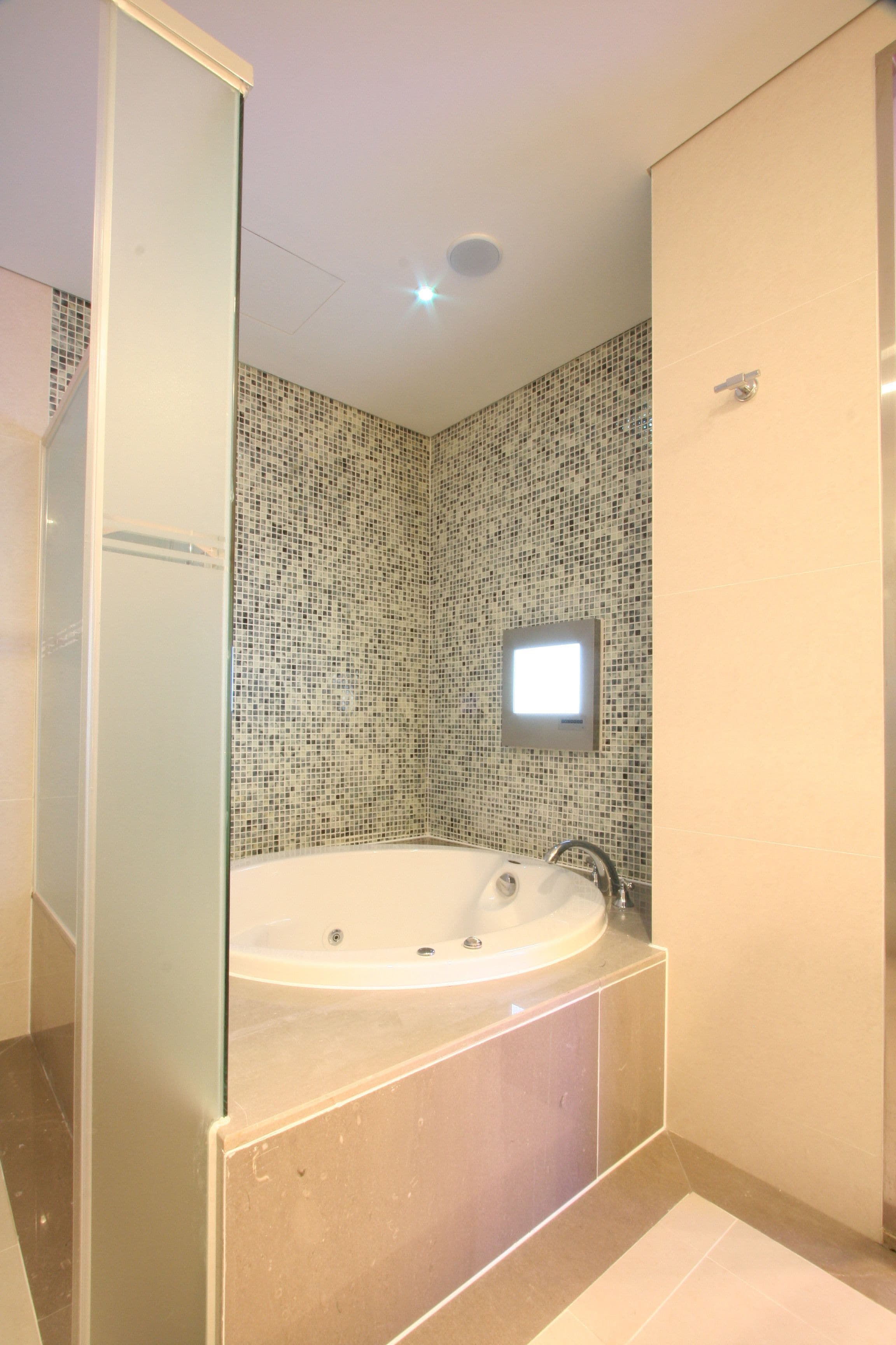 Un baño moderno con una bañera independiente, un espejo pequeño y un muro cubierto de mosaicos.