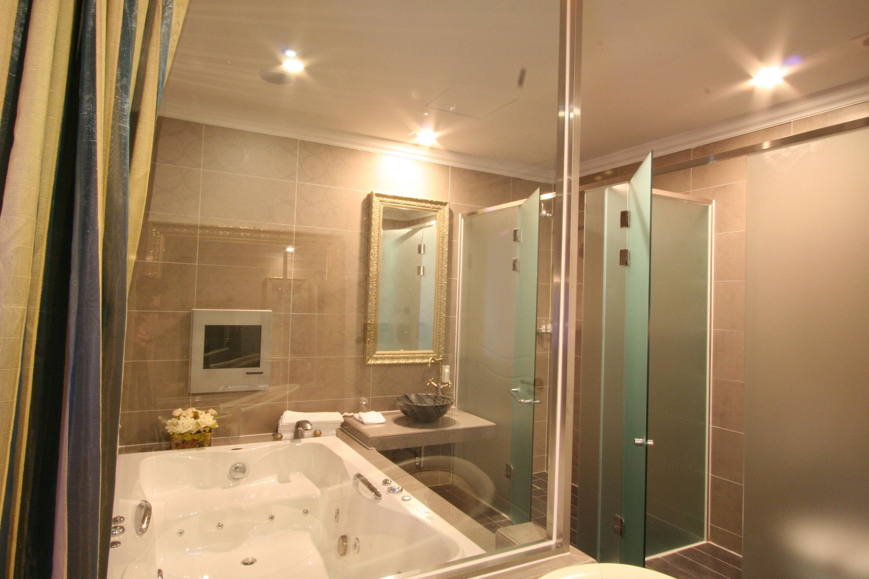Un baño moderno con una bañera grande, ducha con mampara de vidrio y tocador con lavamanos y espejo.