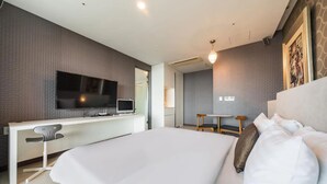 Una habitación de hotel moderna con una cama grande, un escritorio con computadora, televisor y una pequeña mesa con sillas.