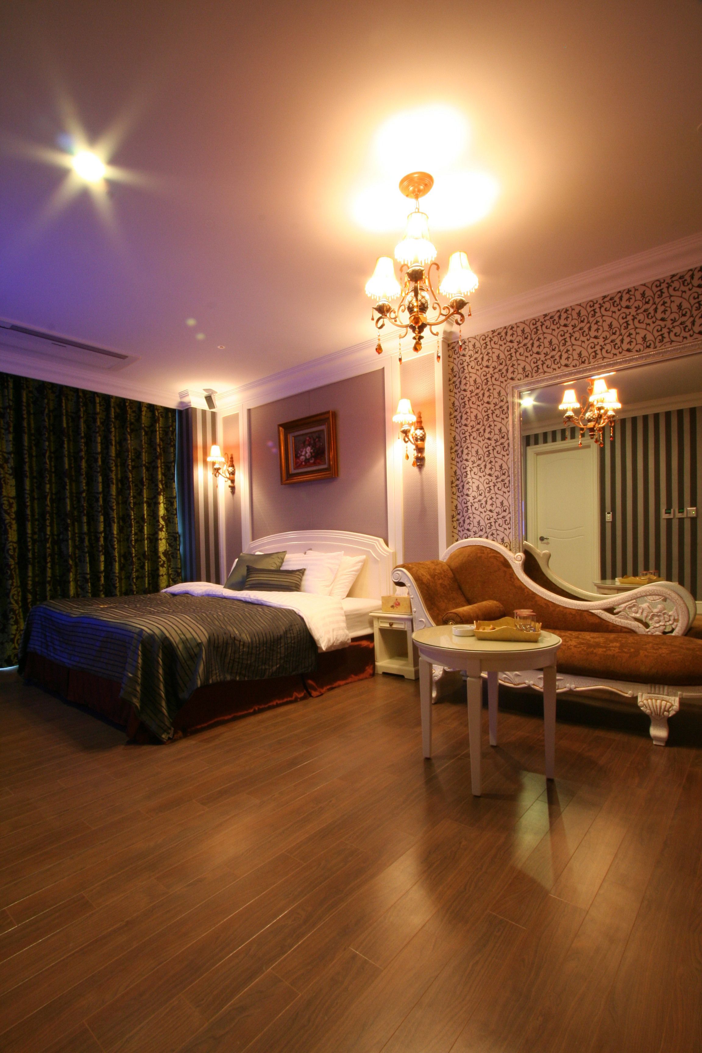 A hotel room with a bed, a sofa, a nightstand, and a chandelier.