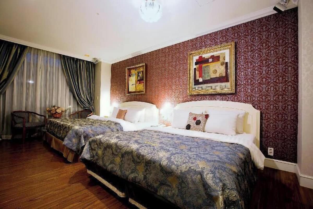 A hotel room with two beds, a chair, a desk, and a large window with curtains.