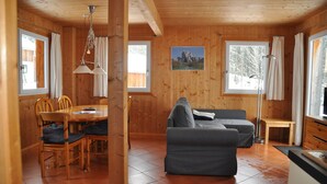 L'intérieur d'un chalet en bois comprend un coin repas, un canapé et de grandes fenêtres.