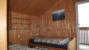 Une pièce de cabane en bois avec deux lits superposés, un plafond en bois, une fenêtre donnant sur les montagnes et une porte menant à l’extérieur.