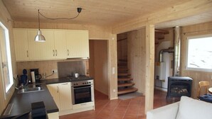 Une cuisine compacte équipée d’une cuisinière, d’un four et d’un évier, un coin repas avec une table et des chaises, et un escalier menant à un niveau supérieur.