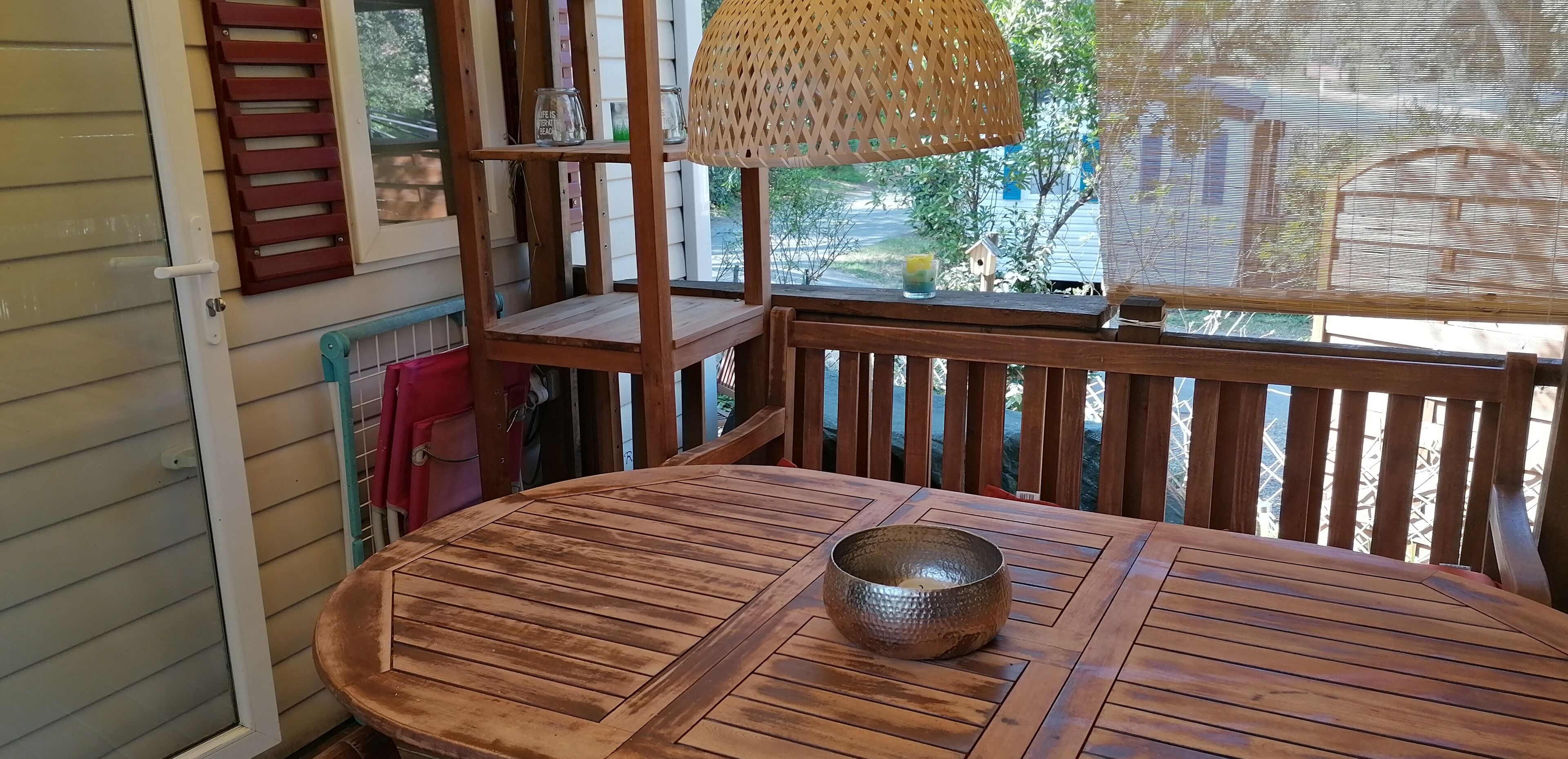 Een houten terras met een ronde tafel en een geweven lamp.