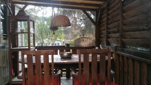 A wooden cabin with a dining area featuring a table and chairs, a hanging light fixture, and a view of the surrounding forest. - SAINT-TROPEZ Bungalow in vacation park with pool - CÔTE D'AZUR  (Gassin)