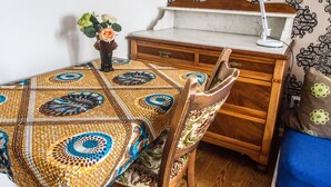 Een kamer met een tafelkleed met patroon, een houten dressoir, een stoel en een bureau met een lamp.