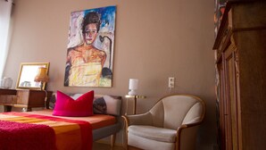 Een slaapkamer met een bed, een stoel, een schilderij aan de muur en een houten kast.