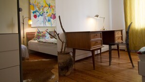 Een slaapkamer met een bed, een bureau, een stoel, een lamp en een vaas met takken.