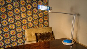 Een houten tafel met een blauwe bureklamp, een kussen met luipaardprint en behang met een patroon.