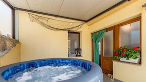 Een hottub met een blauw interieur, een houten deur met geëtste glaspanelen, een groen gordijn en een potplant met rode bloemen.