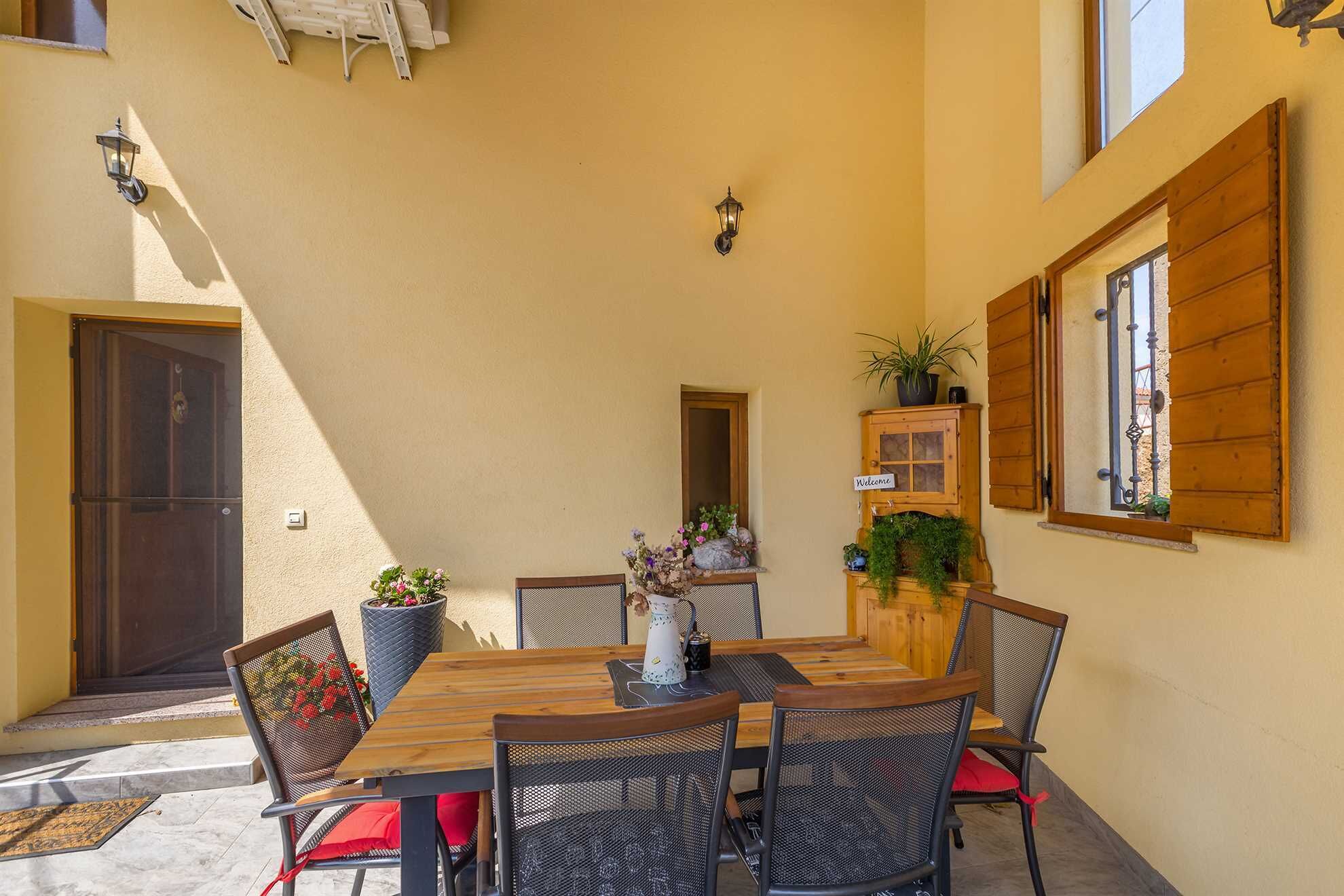 A patio with a wooden table and chairs, a potted plant, and a 'Welcome' sign.