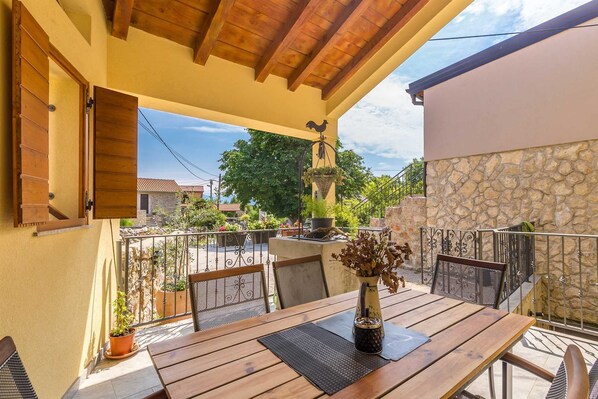 An outdoor patio with a wooden table and chairs, a hanging planter, and a stone wall.
