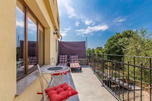 A balcony with a table, chairs, and a red cushion. There is a metal railing and a view of greenery.