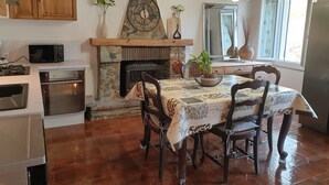 Une cuisine dotée d’une cheminée en pierre, de meubles en bois, d’une table à manger avec des chaises et d’un lustre moderne.