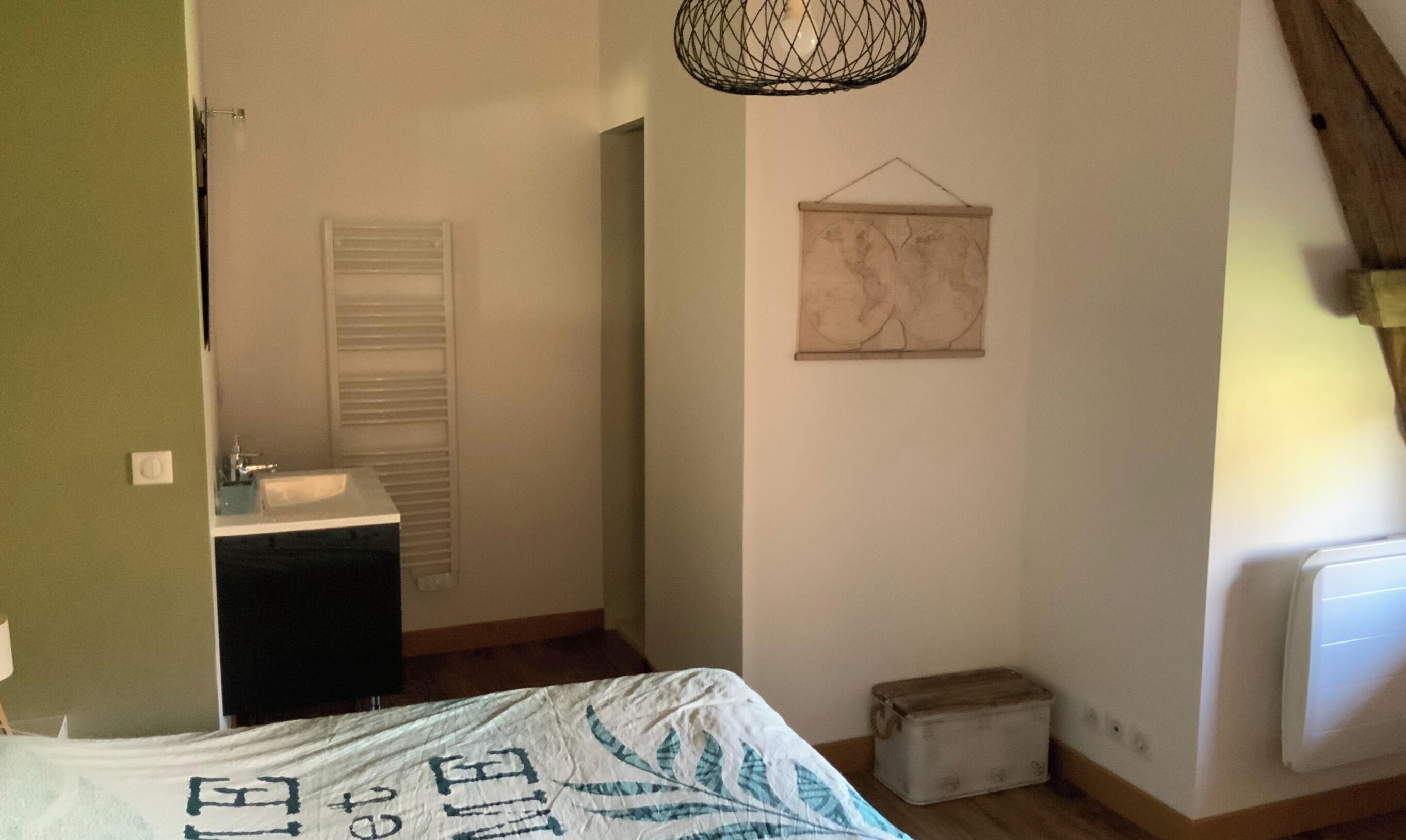 A bedroom with a bed, a dresser, a radiator, a small stool, and a wall-mounted artwork.