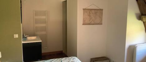 A bedroom with a bed, a dresser, a radiator, a small stool, and a wall-mounted artwork.