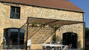 A stone building with a tiled roof, a covered patio with a table and chairs, and a pergola with climbing plants. - Traditional sluice-gate truss hones some on 10 hectares of ground-swimming pool (Gourdon)
