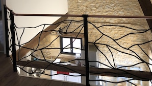 Une pièce avec des poutres apparentes, un mur en pierre et une rambarde en métal au design original.