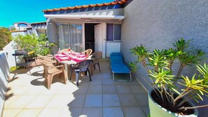 Une petite terrasse avec une table dressée pour deux personnes, un fauteuil bleu et des plantes en pot.