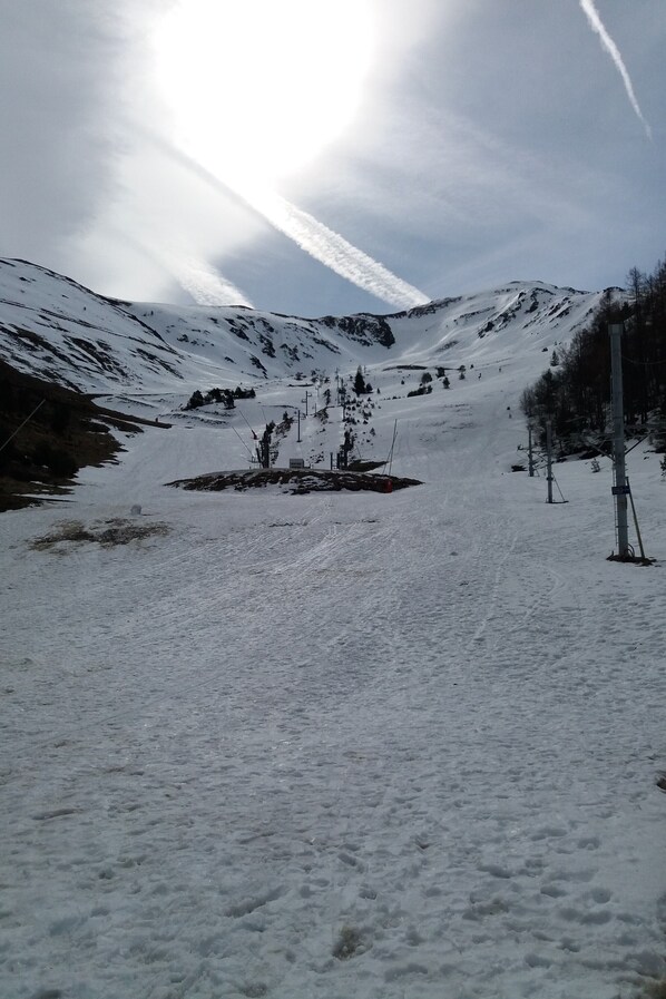 Eine verschneite Berglandschaft mit Skipiste, Skilift und vereinzelten Bäumen.