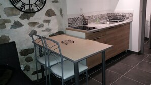 Een kleine keuken met een stenen muur, een moderne klok, een eettafel met stoelen en een decoratieve spatwand.