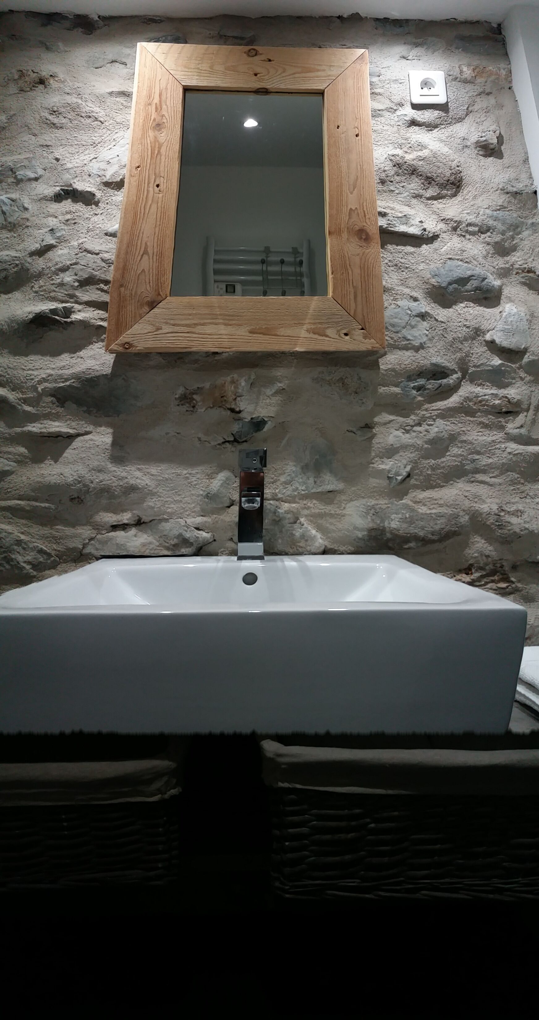 A bathroom with a stone wall, a wooden-framed mirror, and a white sink.